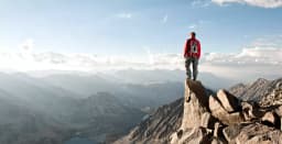 Hiker standing on rocky outcrop, looking at mountains.