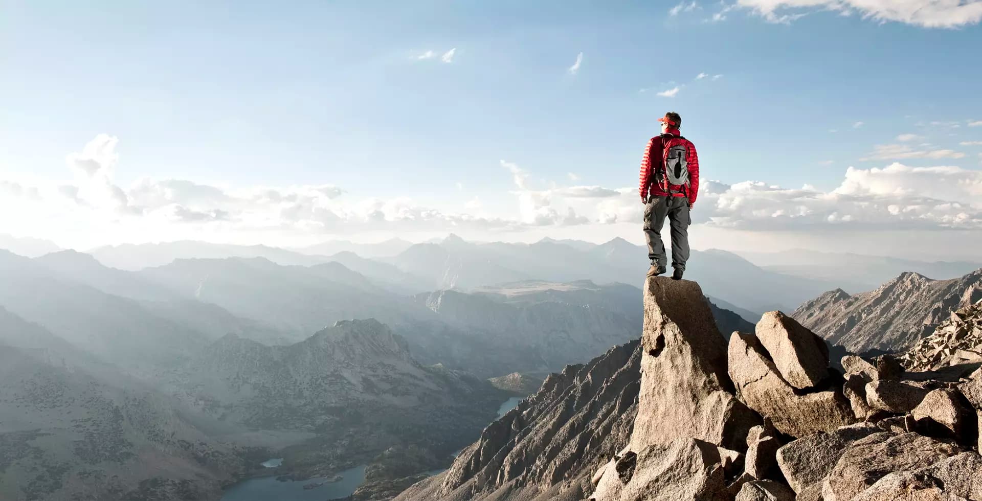 Hiker standing on rocky outcrop, looking at mountains.