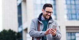 Lächelnder Mann, der draußen sein Handy benutzt.