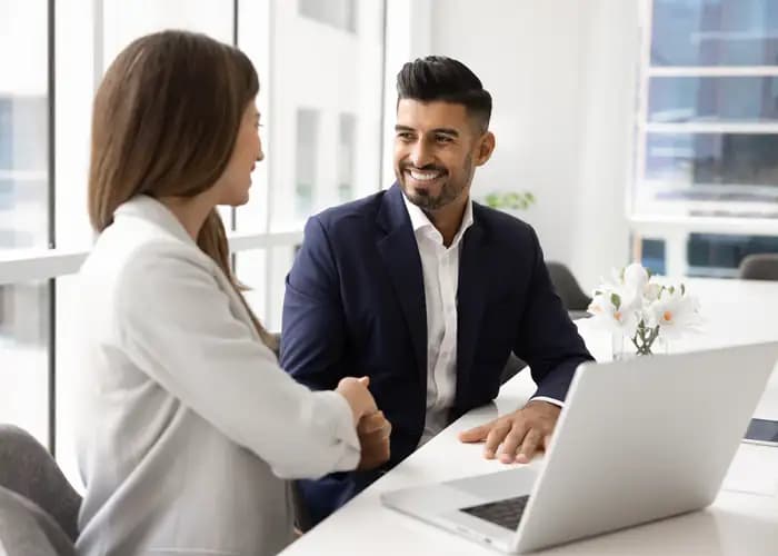 Two colleagues shaking hands across a desk in an office.