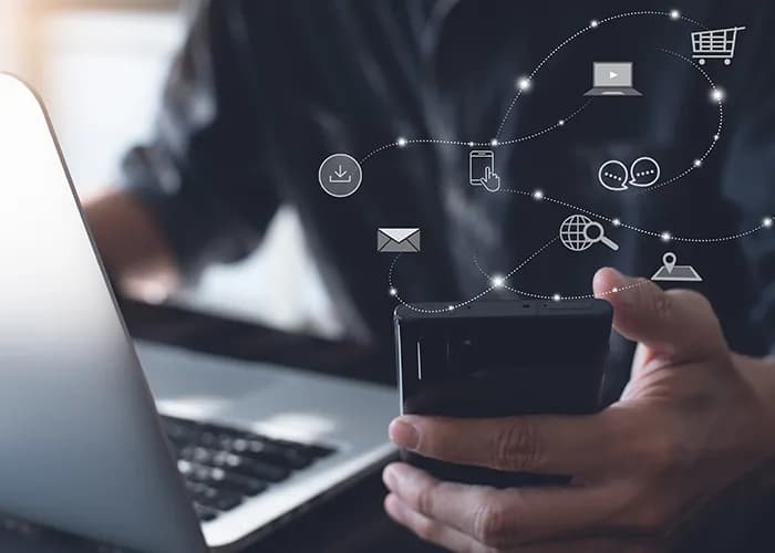 Eine Person, die gleichzeitig Handy und Laptop benutzt.