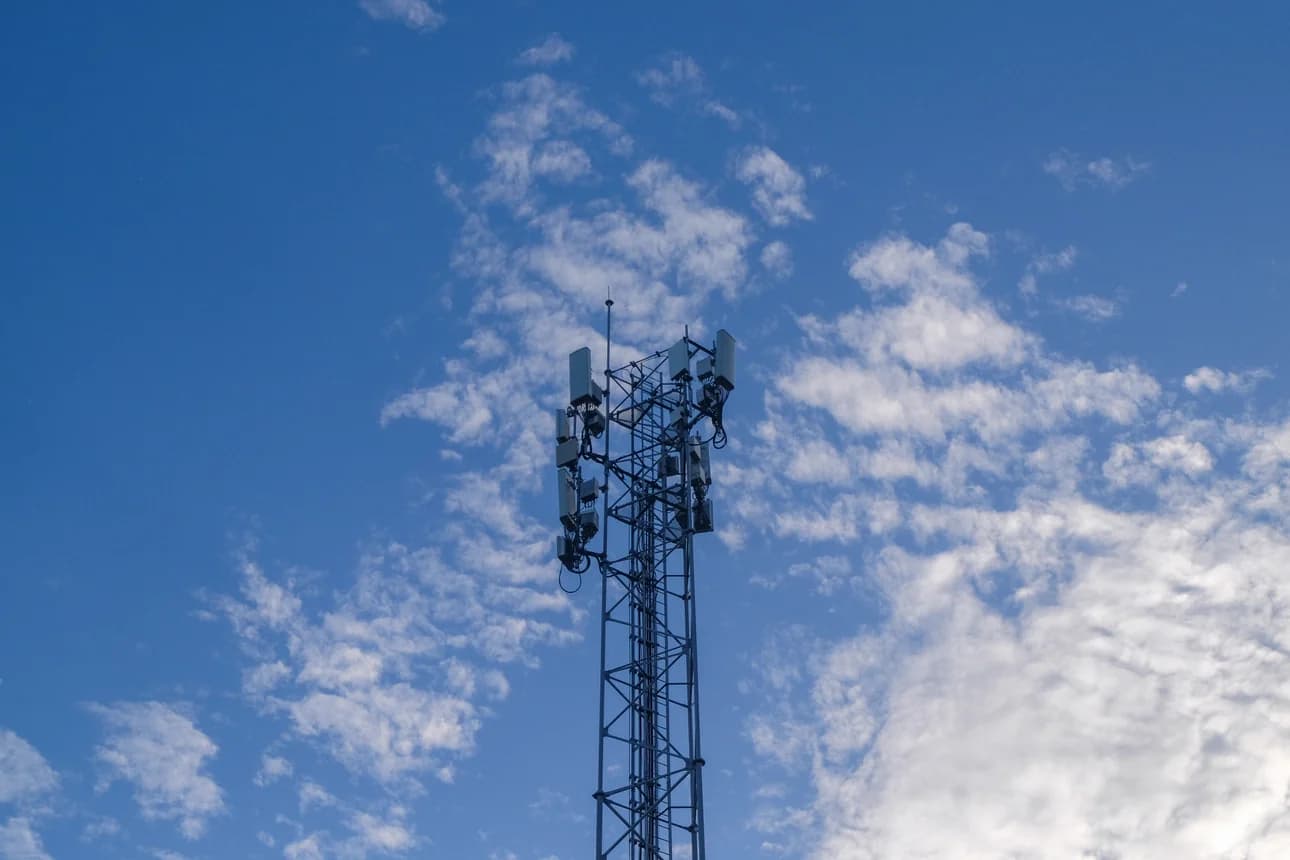 A tall mobile phone mast against a blue sky with white clouds.