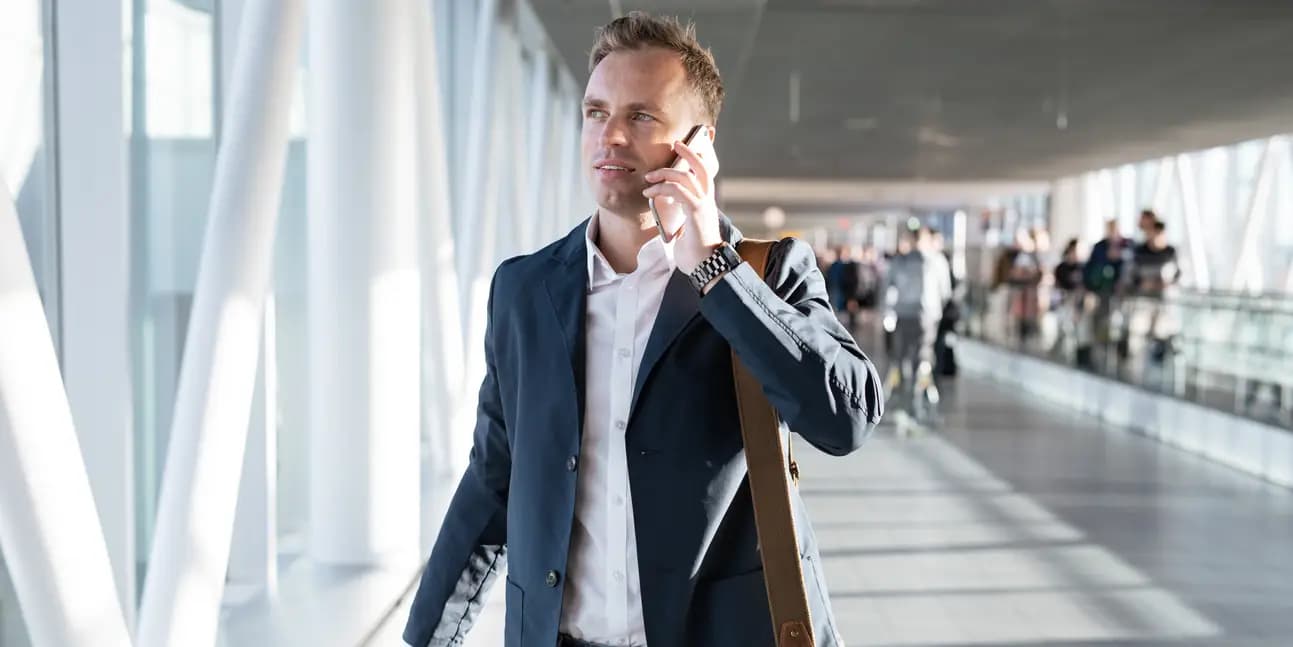 A business traveller talking on a mobile phone while walking through an airport terminal.