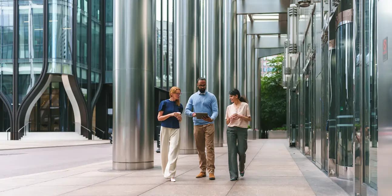 Three colleagues walking and talking together outside a modern glass office building.