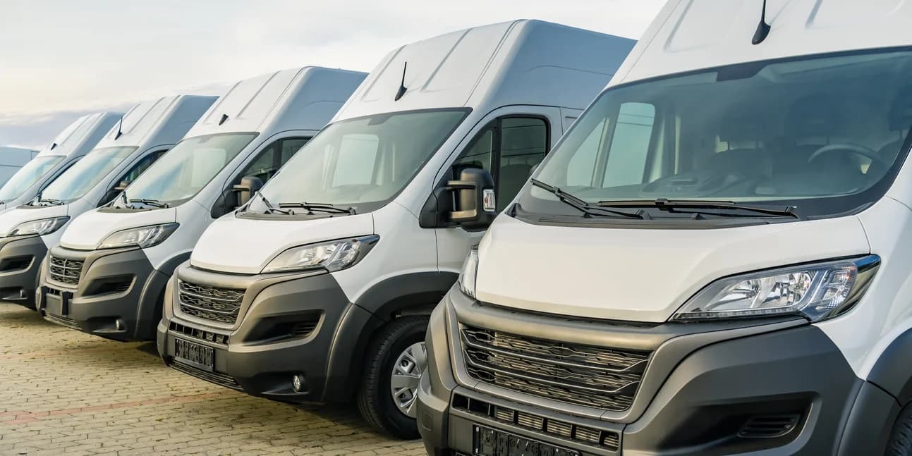 A row of white delivery vans parked side by side on a depot forecourt.