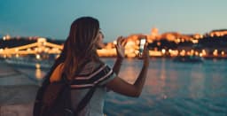 Jeune voyageur utilisant un téléphone au bord d'une rivière urbaine la nuit.