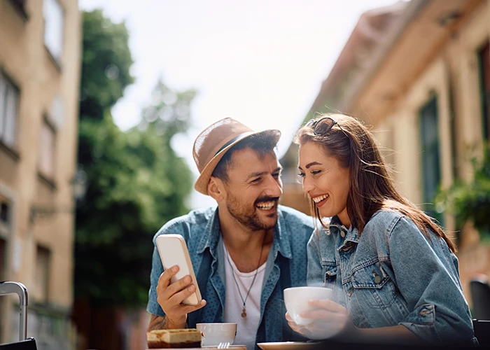 image of a happy couple using a cell phone while drinking coffee in a city